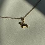 Ein goldener Hunde Anhänger an einer goldenen Kette liegt auf einem weißem Leinentuch. 