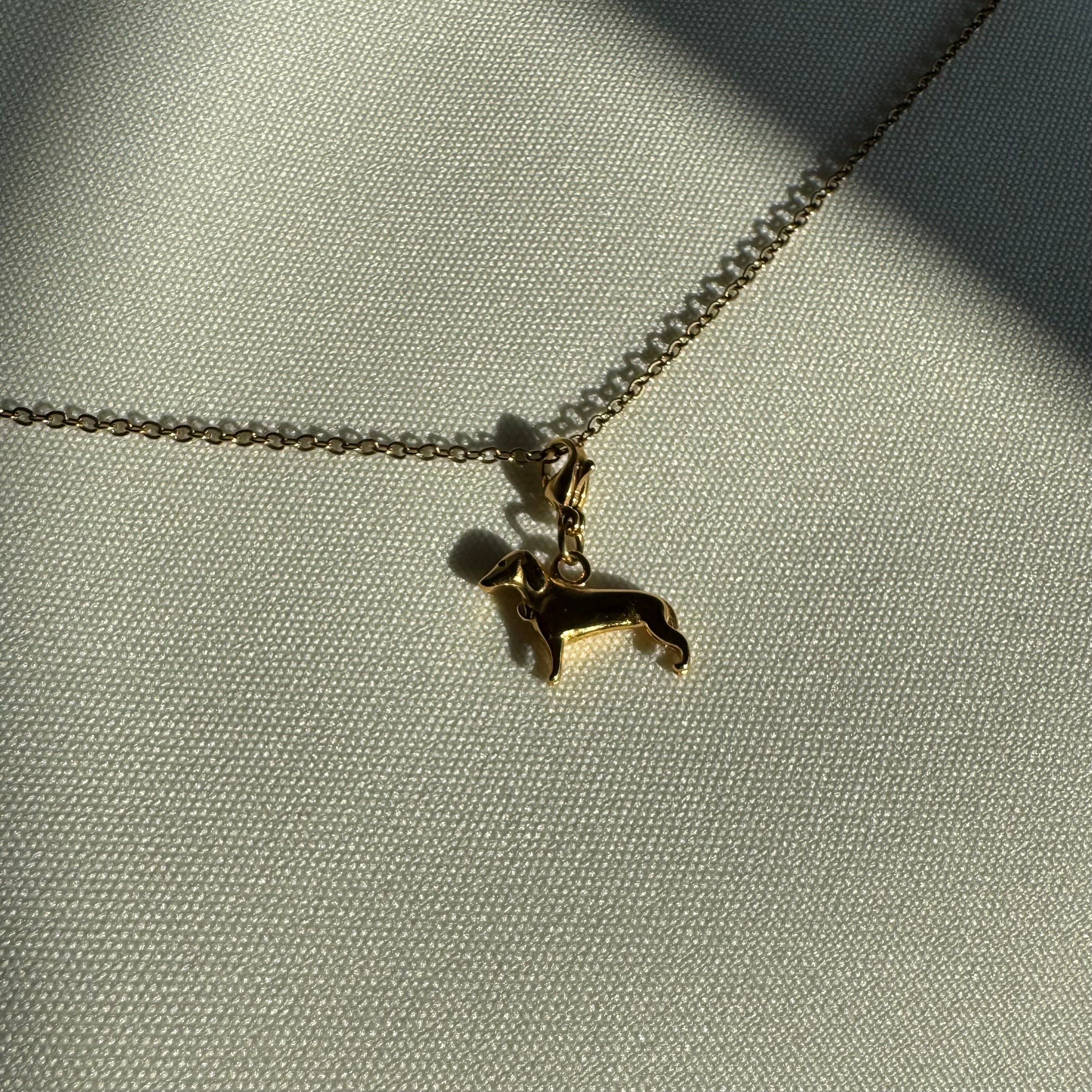 Ein goldener Hunde Anhänger an einer goldenen Kette liegt auf einem weißem Leinentuch. 