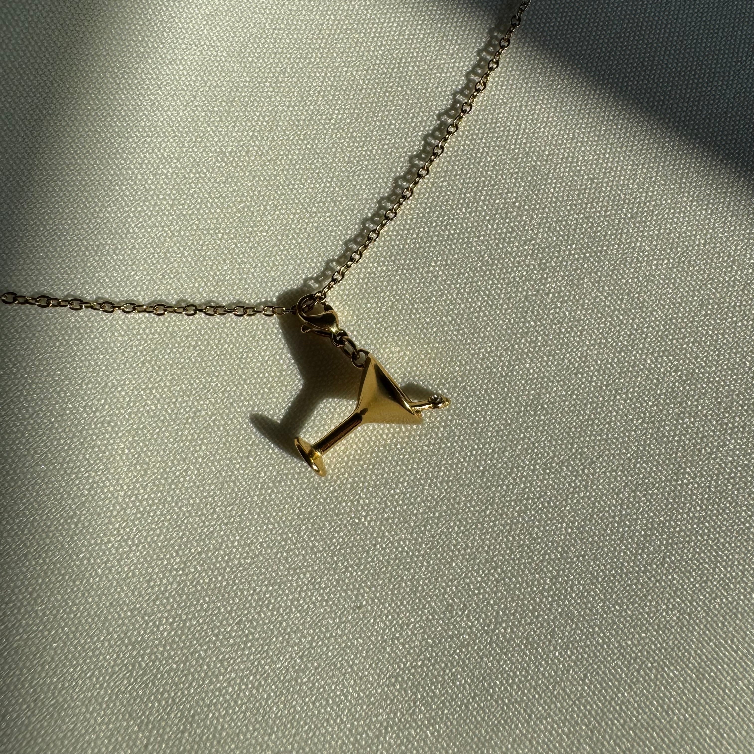 Goldener Cocktail Charm auf Seidentuch im Sonnenlicht