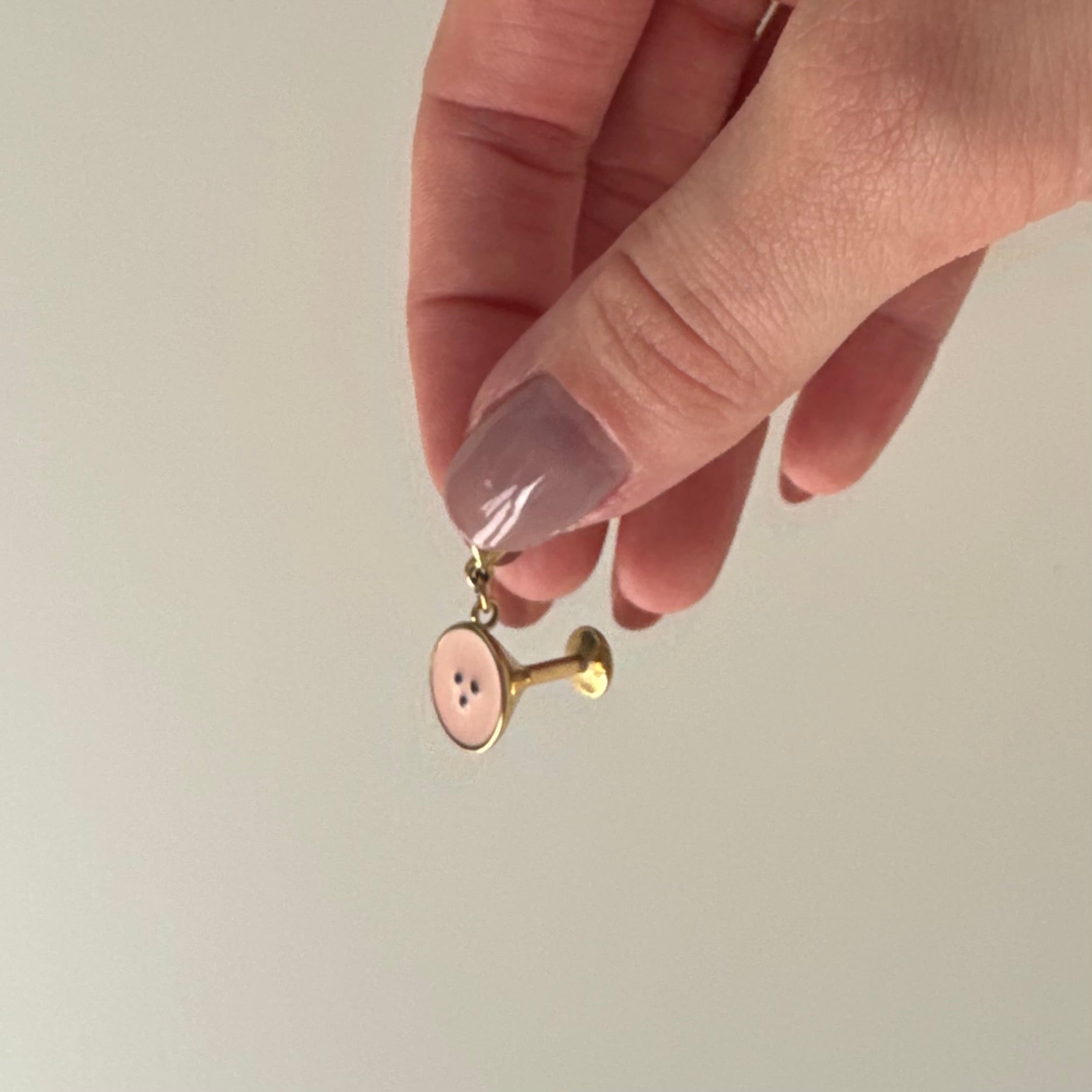 Ein goldener Espresso Martini Charm wird in den Fingern gehalten und baumelt vor weißem Hintergrund. 