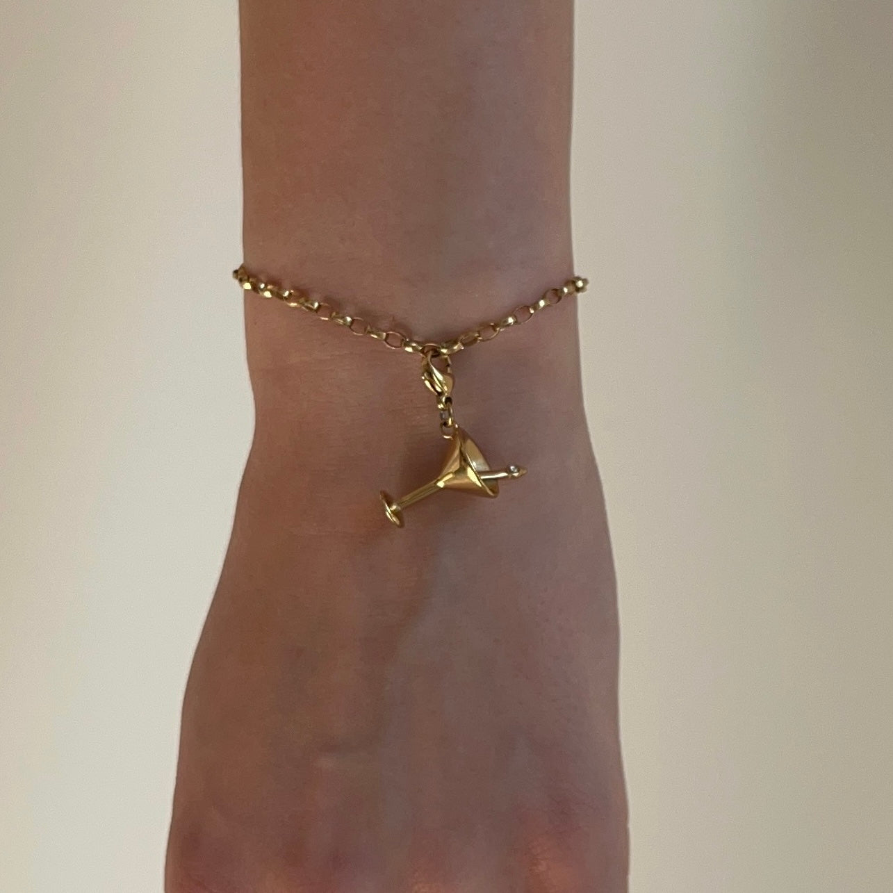 Goldener Cocktail Charm an Armband am Handgelenk vor weißem Hintergrund