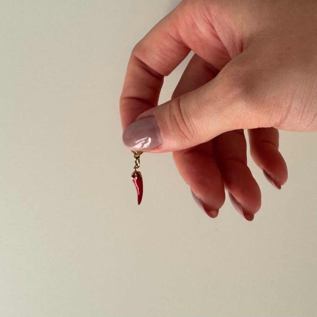 Rot goldener Anhänger wird zwischen Daumen und Zeigefinger gehalten und baumelt vor weißem Hintergrund. 