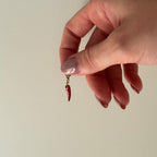 Rot goldener Anhänger wird zwischen Daumen und Zeigefinger gehalten und baumelt vor weißem Hintergrund. 