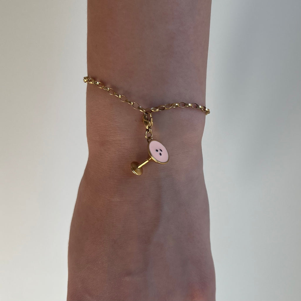 Ein goldener Anhänger in Form eines Espresso Martini hängt an einem goldenen Armband das an einem Arm befestigt ist. 