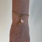 Ein goldener Anhänger in Form eines Espresso Martini hängt an einem goldenen Armband das an einem Arm befestigt ist. 