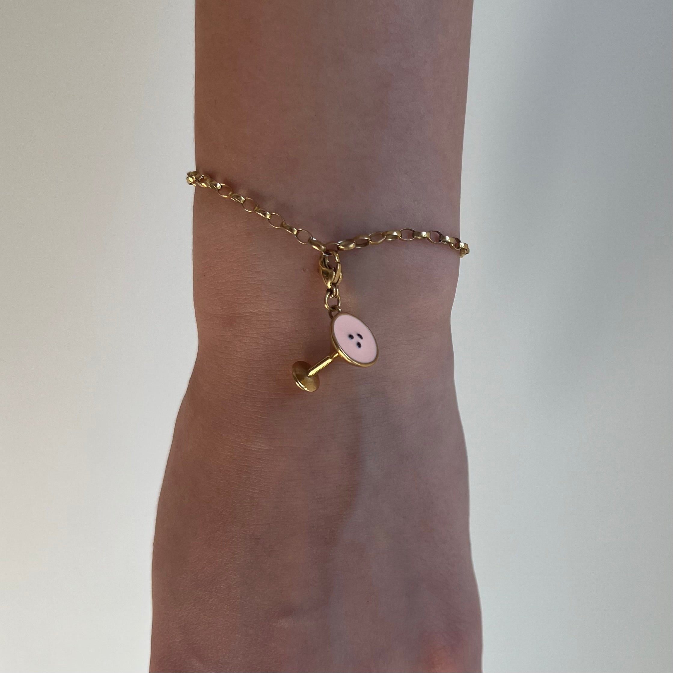 Ein goldener Anhänger in Form eines Espresso Martini hängt an einem goldenen Armband das an einem Arm befestigt ist. 