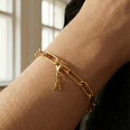 Charm A in gold hängt an goldenem Armband am Handgelenk. Im Hintergrund stylische Altbauwohnung