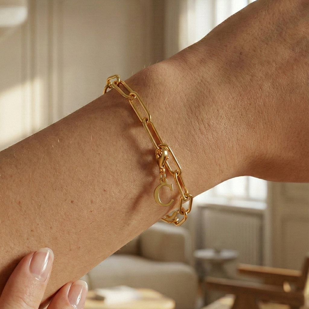 Charm C  in gold hängt an goldenem Armband am Handgelenk. Im Hintergrund stylische Altbauwohnung