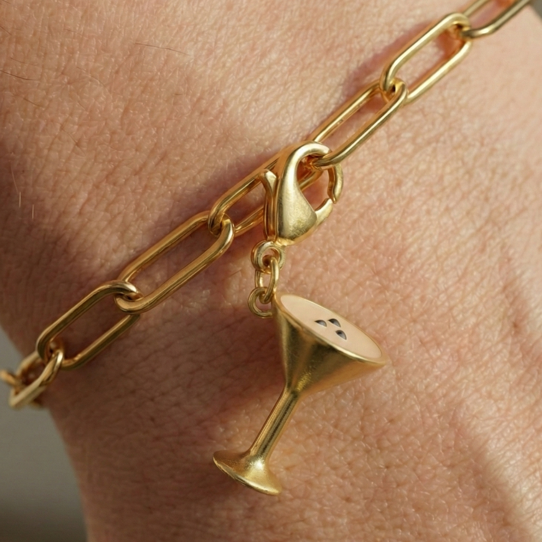 Charm Espresso Martini in gold hängt an goldenem Armband am Handgelenk als Nahaufnahme.