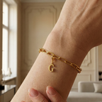 Charm G in gold hängt an goldenem Armband am Handgelenk. Im Hintergrund stylische Altbauwohnung