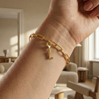 Charm L in gold hängt an goldenem Armband am Handgelenk. Im Hintergrund stylische Altbauwohnung