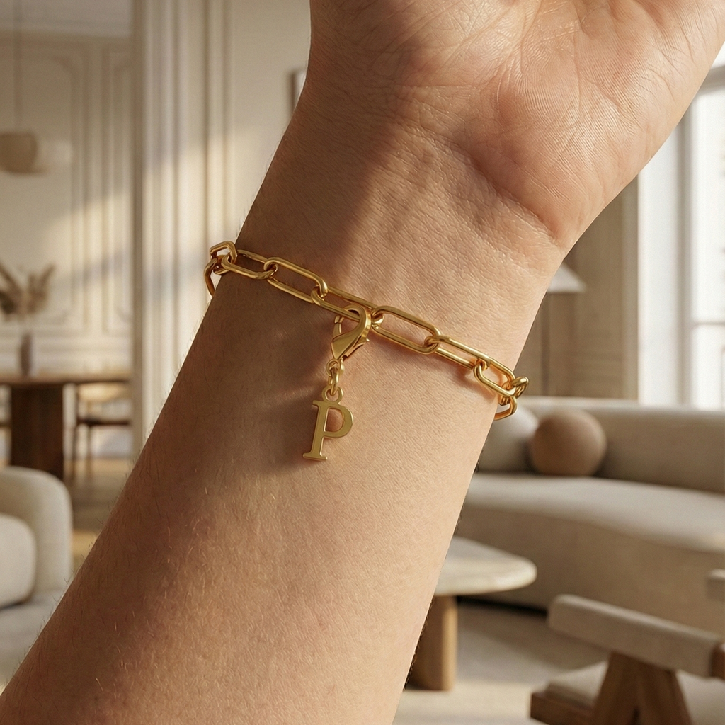 Charm P in gold hängt an goldenem Armband am Handgelenk. Im Hintergrund stylische Altbauwohnung
