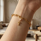 Charm T in gold hängt an goldenem Armband am Handgelenk. Im Hintergrund stylische Altbauwohnung