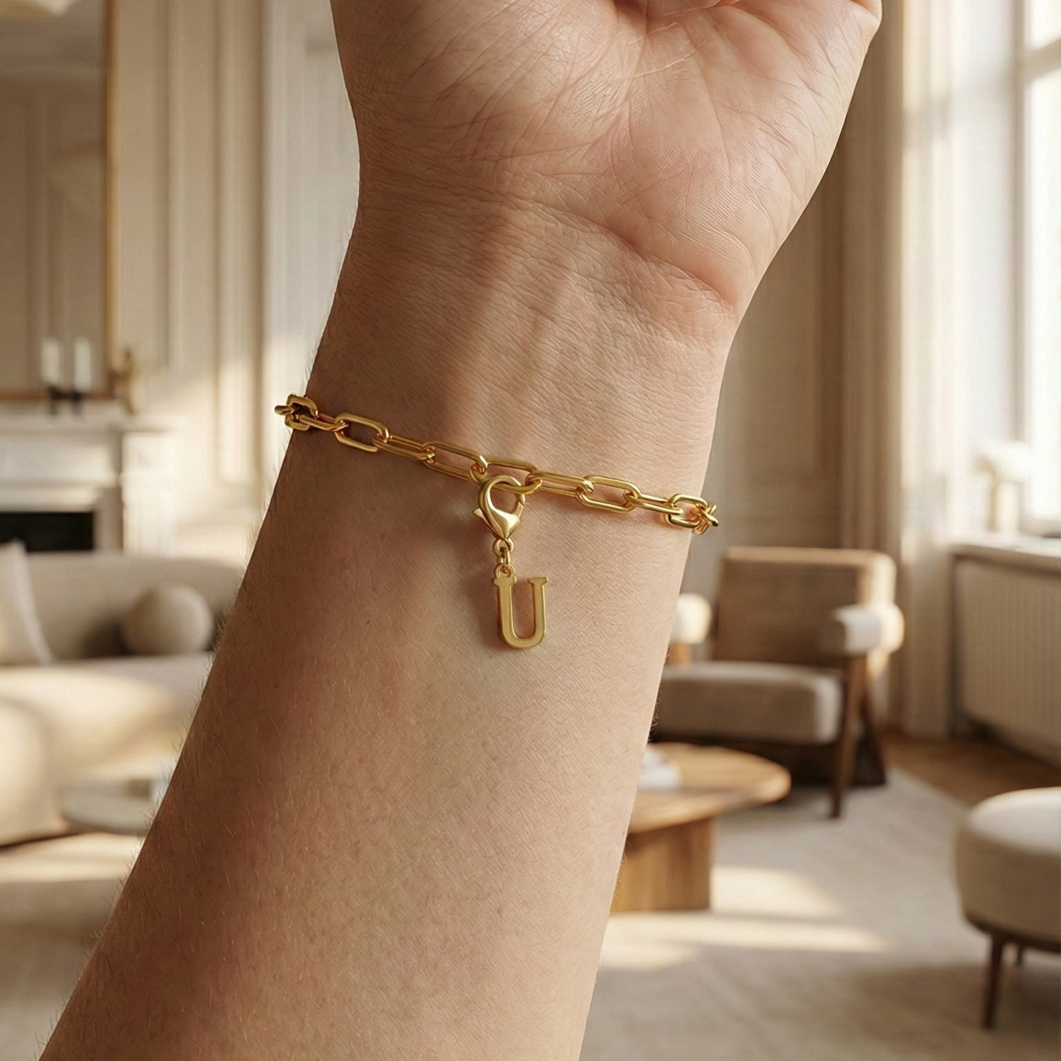 Charm U in gold hängt an goldenem Armband am Handgelenk. Im Hintergrund stylische Altbauwohnung