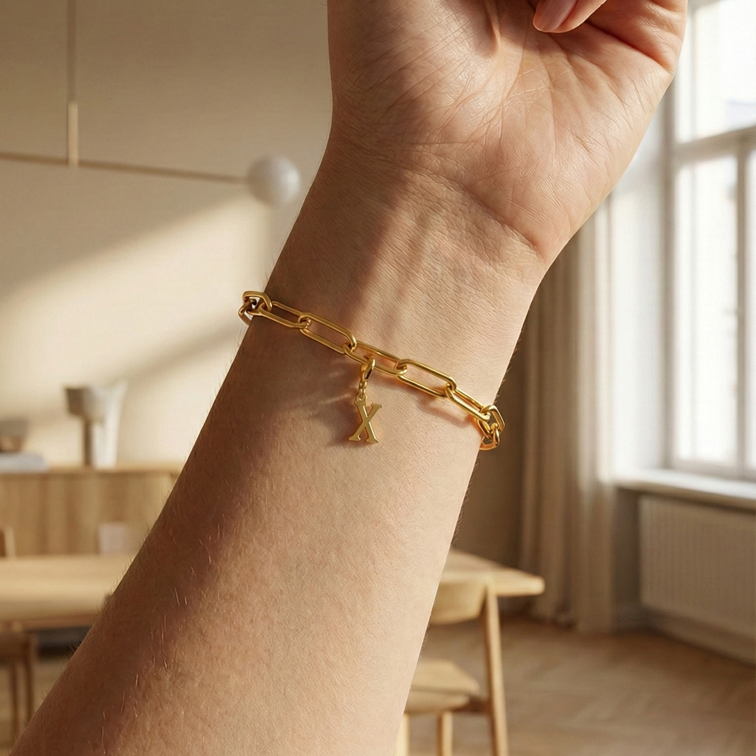 Charm X in gold hängt an goldenem Armband am Handgelenk. Im Hintergrund stylische Altbauwohnung