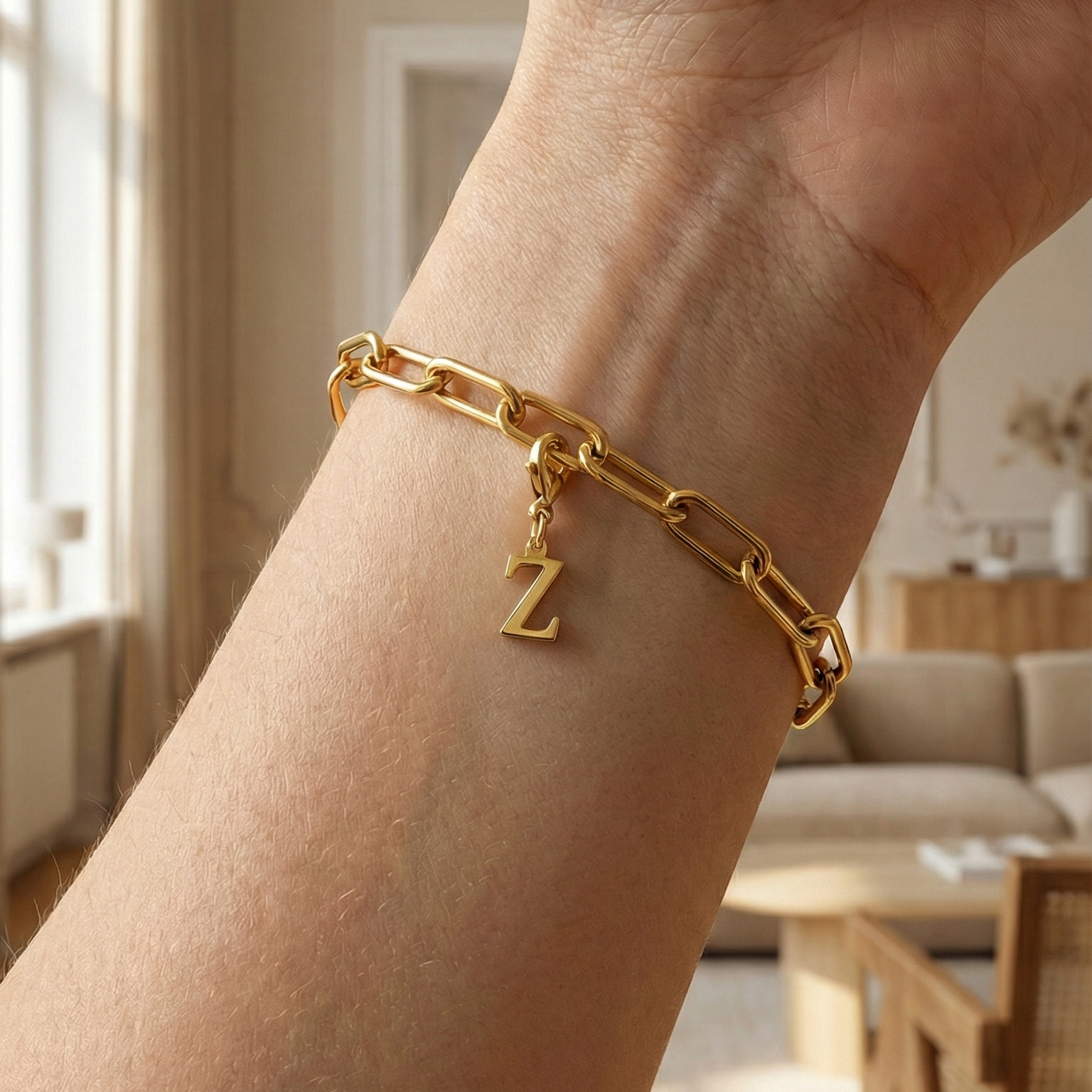 Charm Z in gold hängt an goldenem Armband am Handgelenk. Im Hintergrund stylische Altbauwohnung