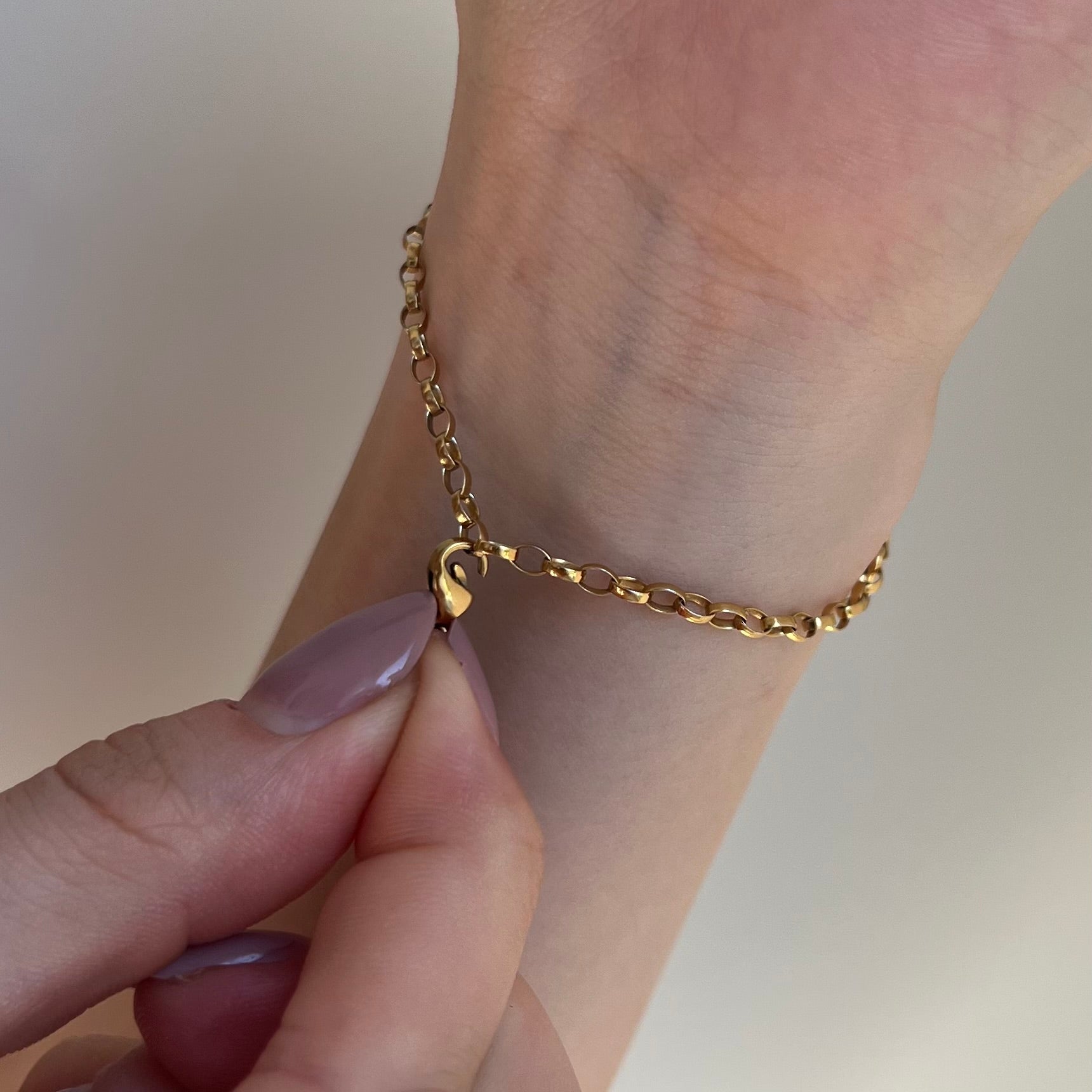 Goldener Anhänger in den Fingerspitzen wird an goldenem Armband am Handgelenk befestigt vor weißem Hintergrund