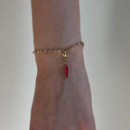 Rot goldener Chili Charm an goldenem Armband ist an einem Handgelenk vor weißem Hintergrund. 