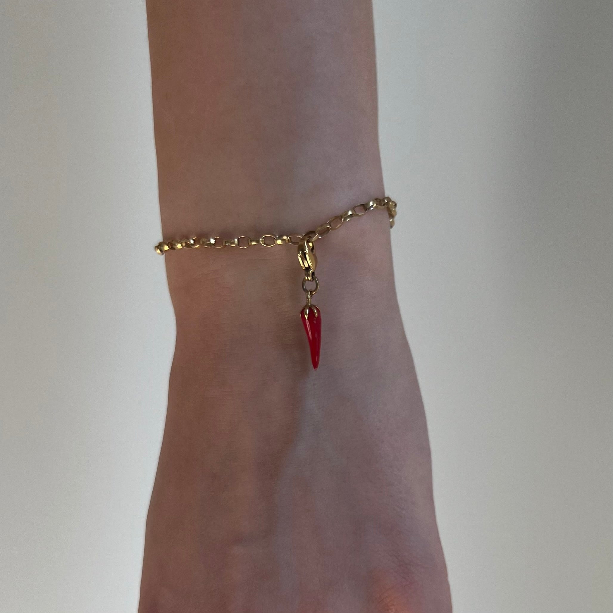 Rot goldener Chili Charm an goldenem Armband ist an einem Handgelenk vor weißem Hintergrund. 