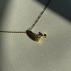 Ein goldener Espresso Martini Anhänger an einer goldenen Kette liegt auf einem weißen Leinentuch. 