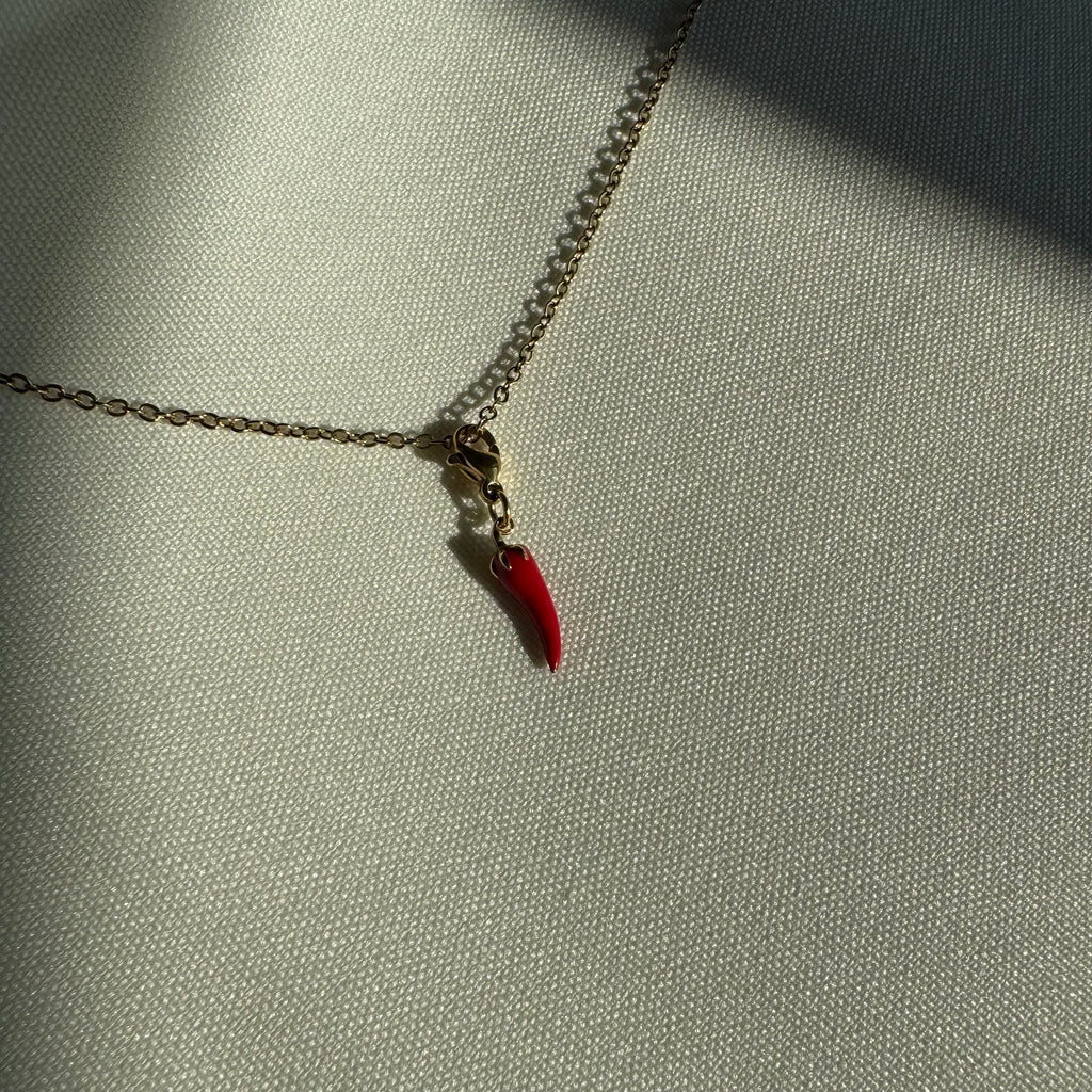 Rot goldener Chili Anhänger an einer goldenen Kette liegt auf einem weißen Leinentuch. 