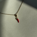 Rot goldener Chili Anhänger an einer goldenen Kette liegt auf einem weißen Leinentuch. 