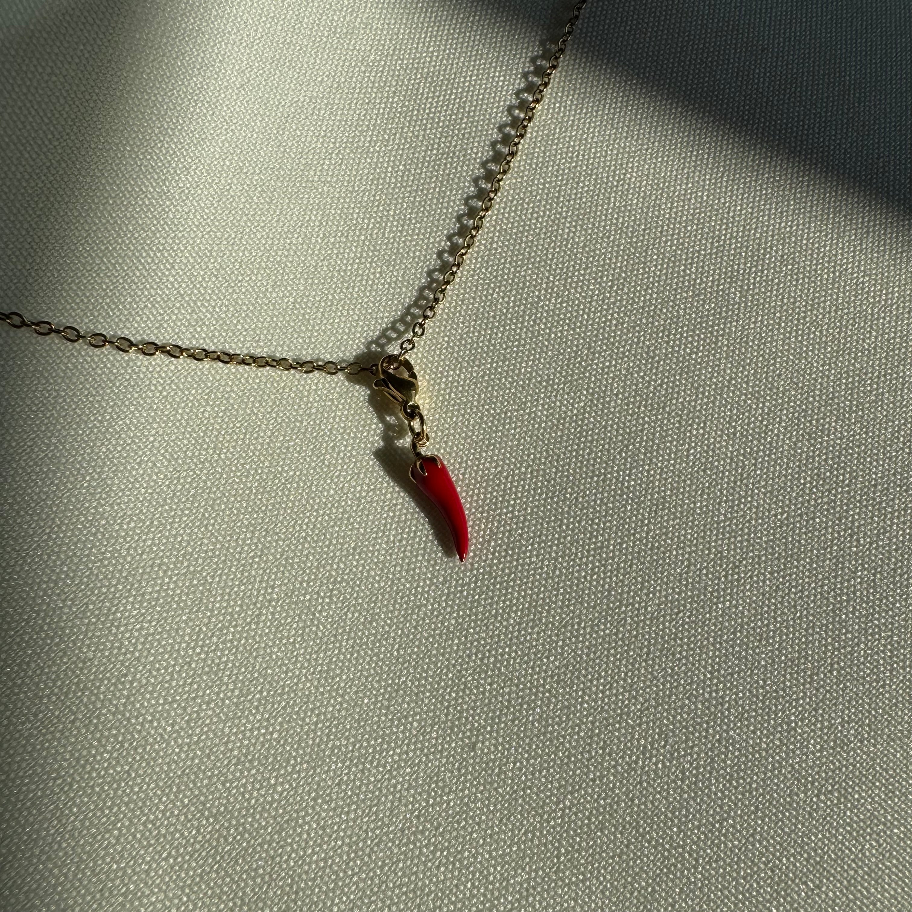 Rot goldener Chili Anhänger an einer goldenen Kette liegt auf einem weißen Leinentuch. 