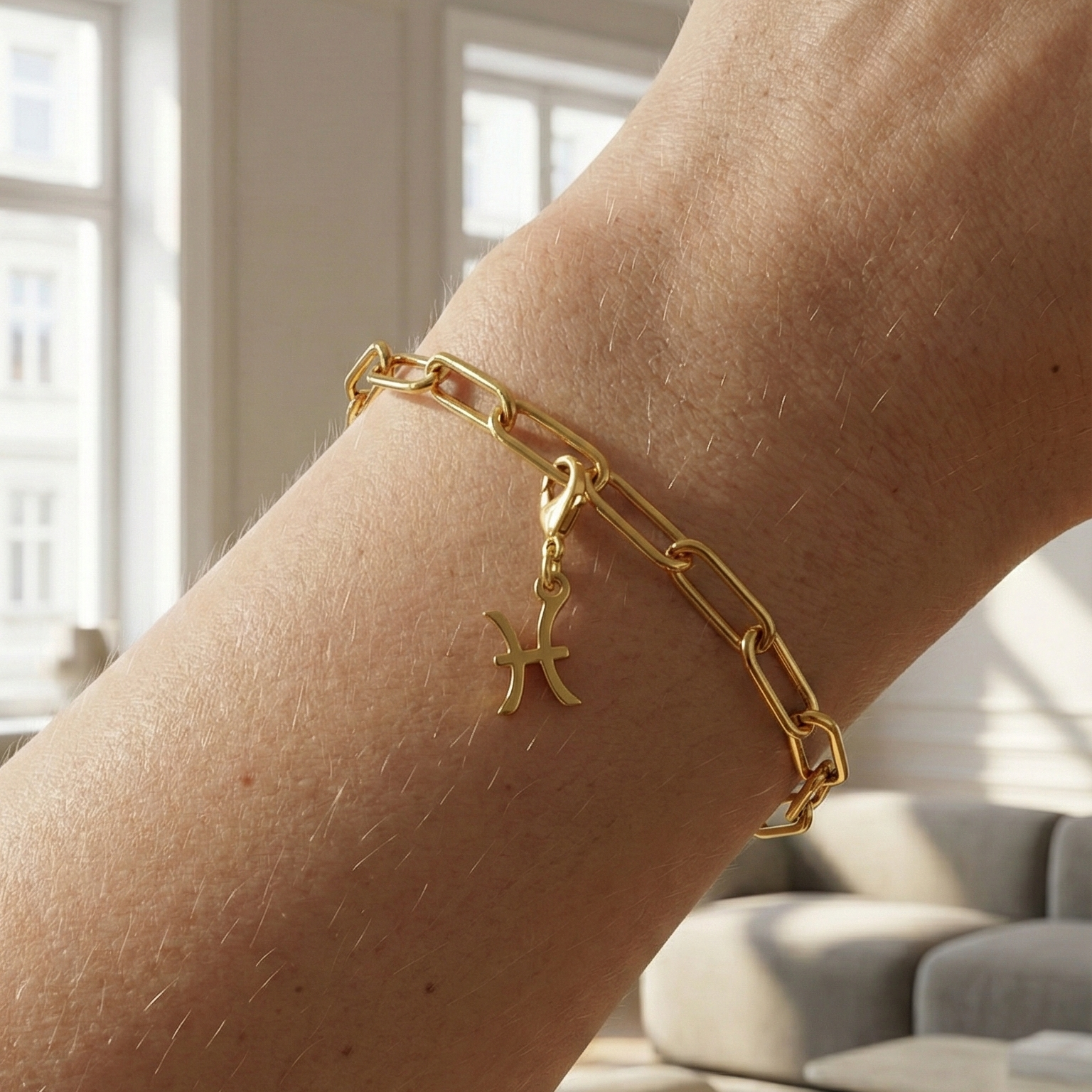 Charm Sternzeichen Fische in gold hängt an goldenem Armband am Handgelenk. Im Hintergrund stylische Altbauwohnung
