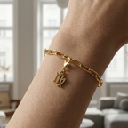 Charm Sternzeichen Jungfrau in gold hängt an goldenem Armband am Handgelenk. Im Hintergrund stylische Altbauwohnung