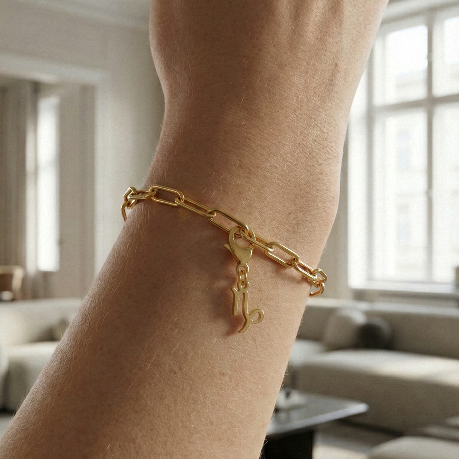 Charm Sternzeichen Steinbock in gold hängt an goldenem Armband am Handgelenk. Im Hintergrund stylische Altbauwohnung