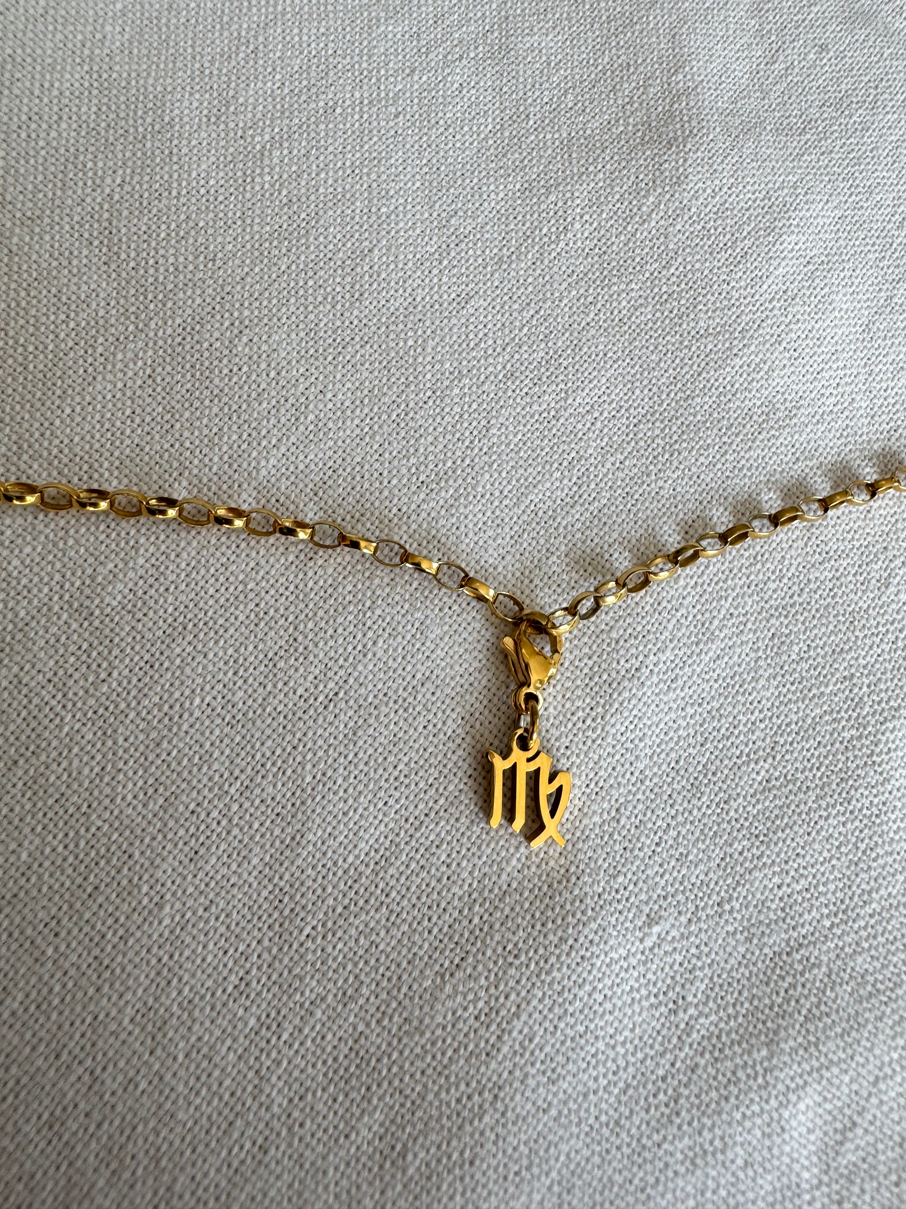 Goldener Jungfrau Sternzeichen Charm an  goldenem Armband liegt auf weißem Leinentuch