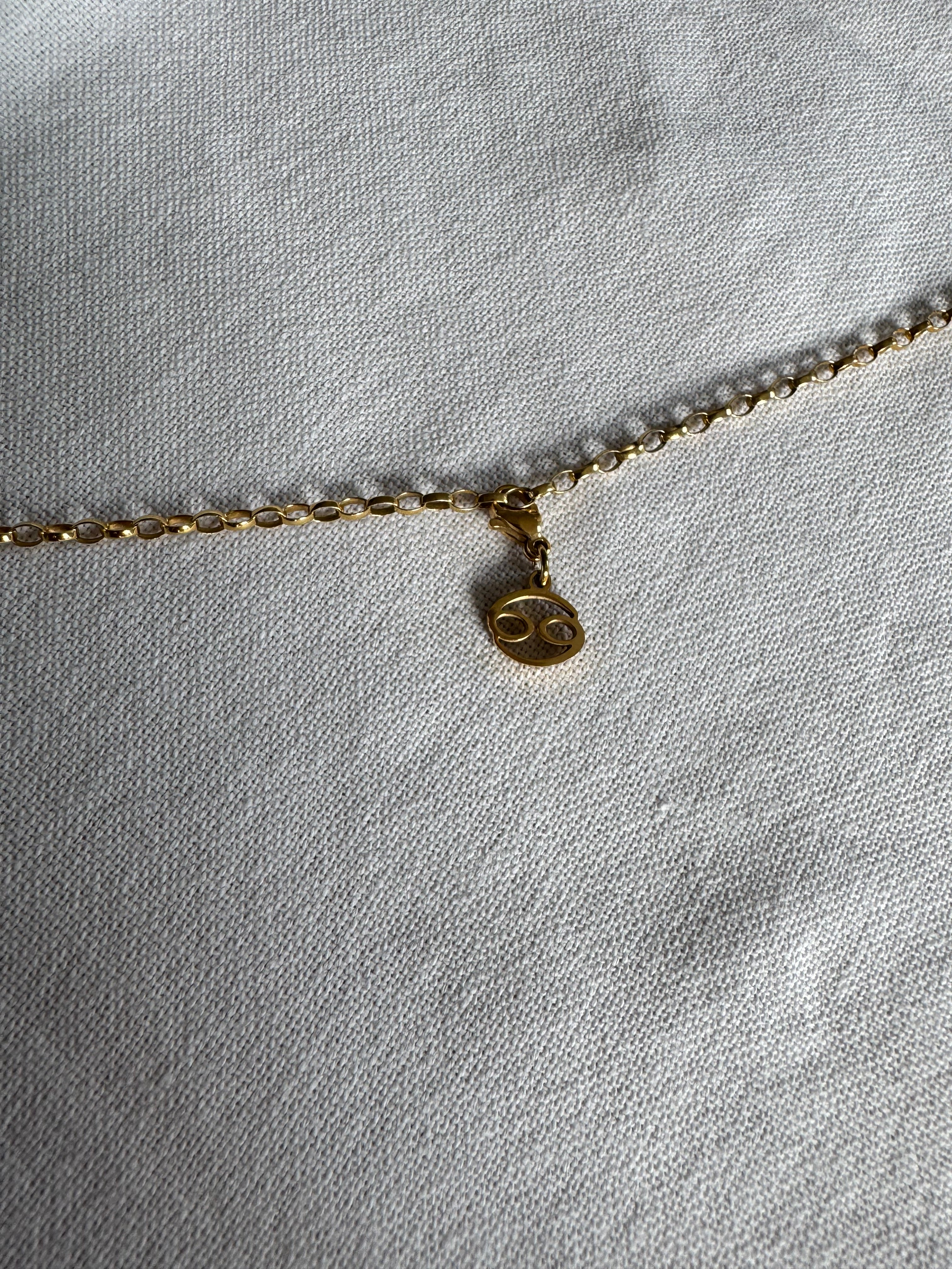 Goldener Krebs Sternzeichen Charm an  goldenem Armband liegt auf weißem Leinentuch
