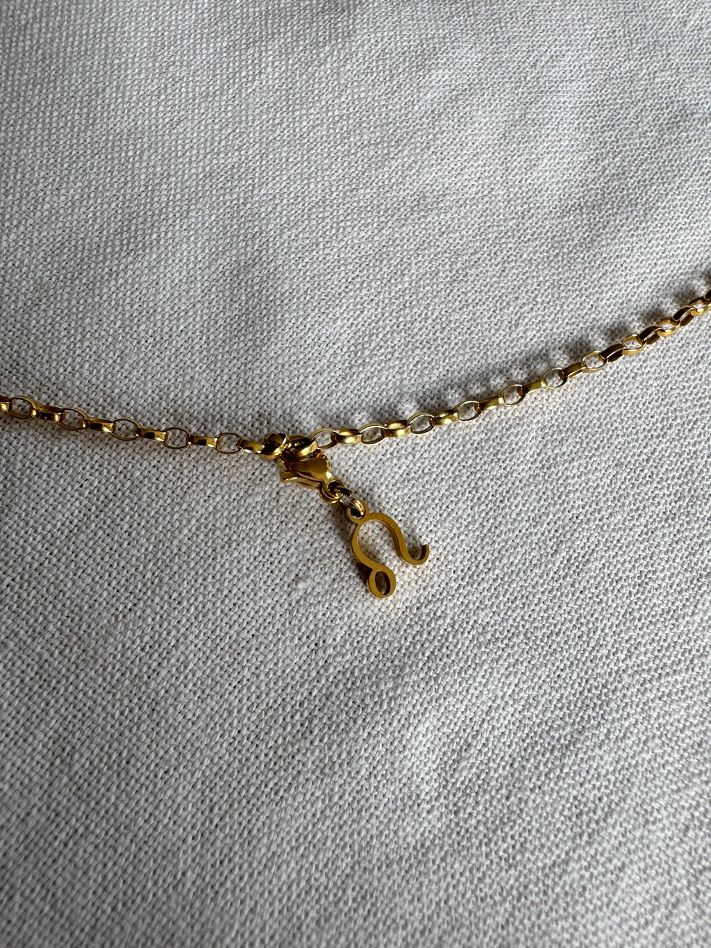 Goldener Löwe Sternzeichen Charm an  goldenem Armband liegt auf weißem Leinentuch