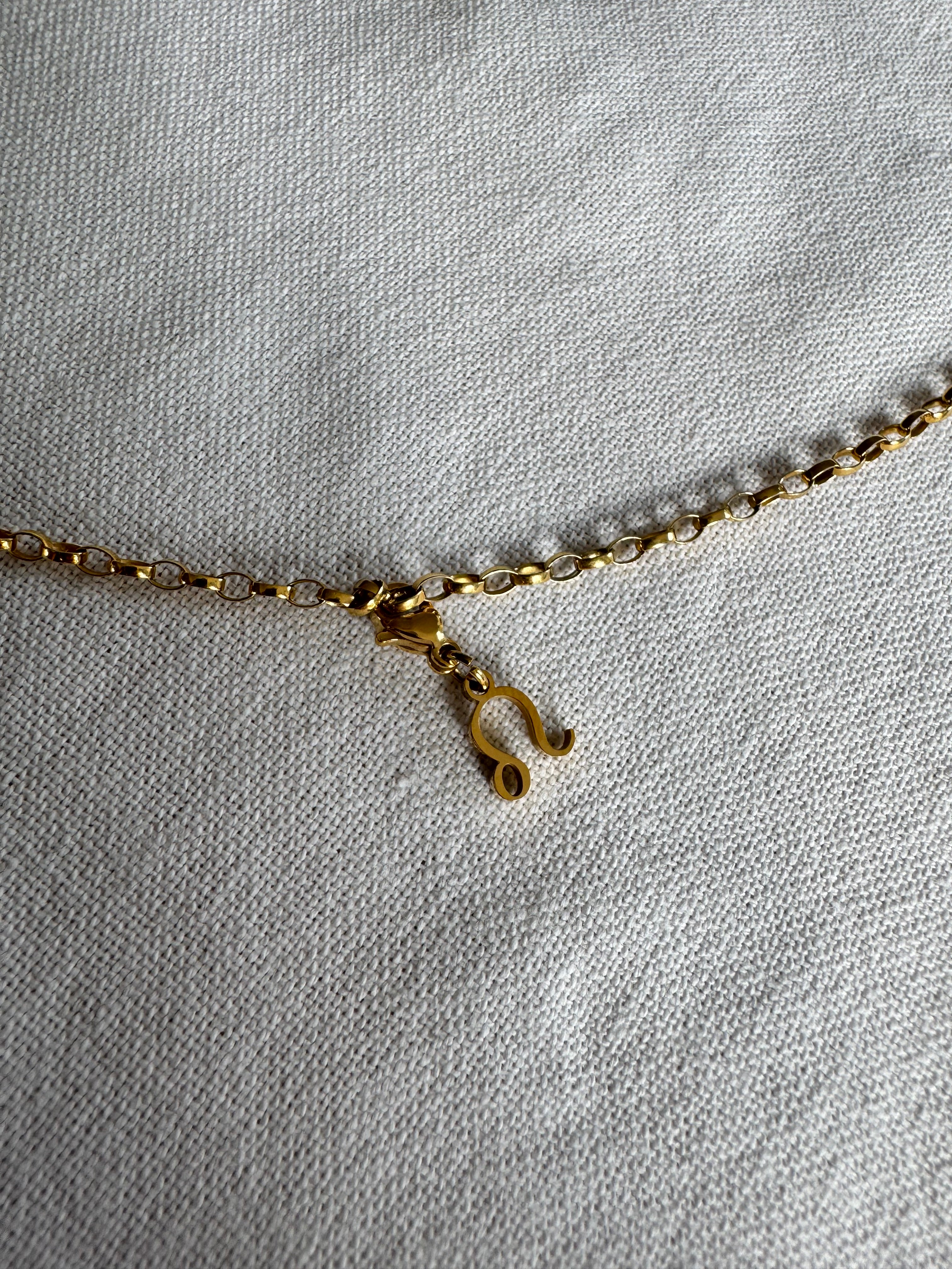 Goldener Löwe Sternzeichen Charm an  goldenem Armband liegt auf weißem Leinentuch