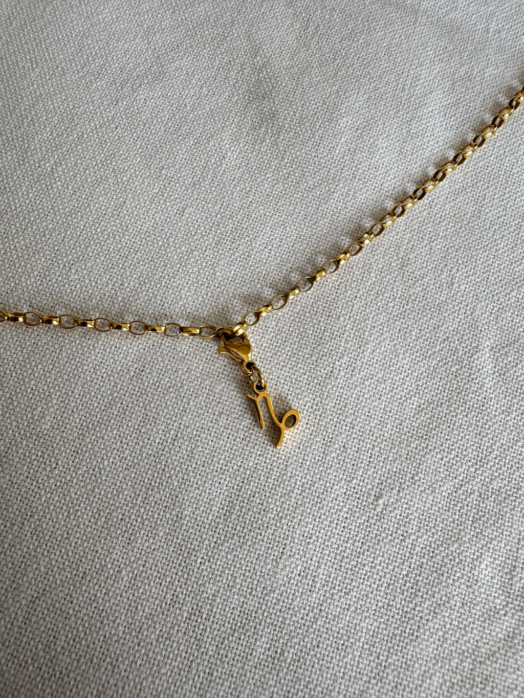Goldener Steinbock Sternzeichen Charm an  goldenem Armband liegt auf weißem Leinentuch