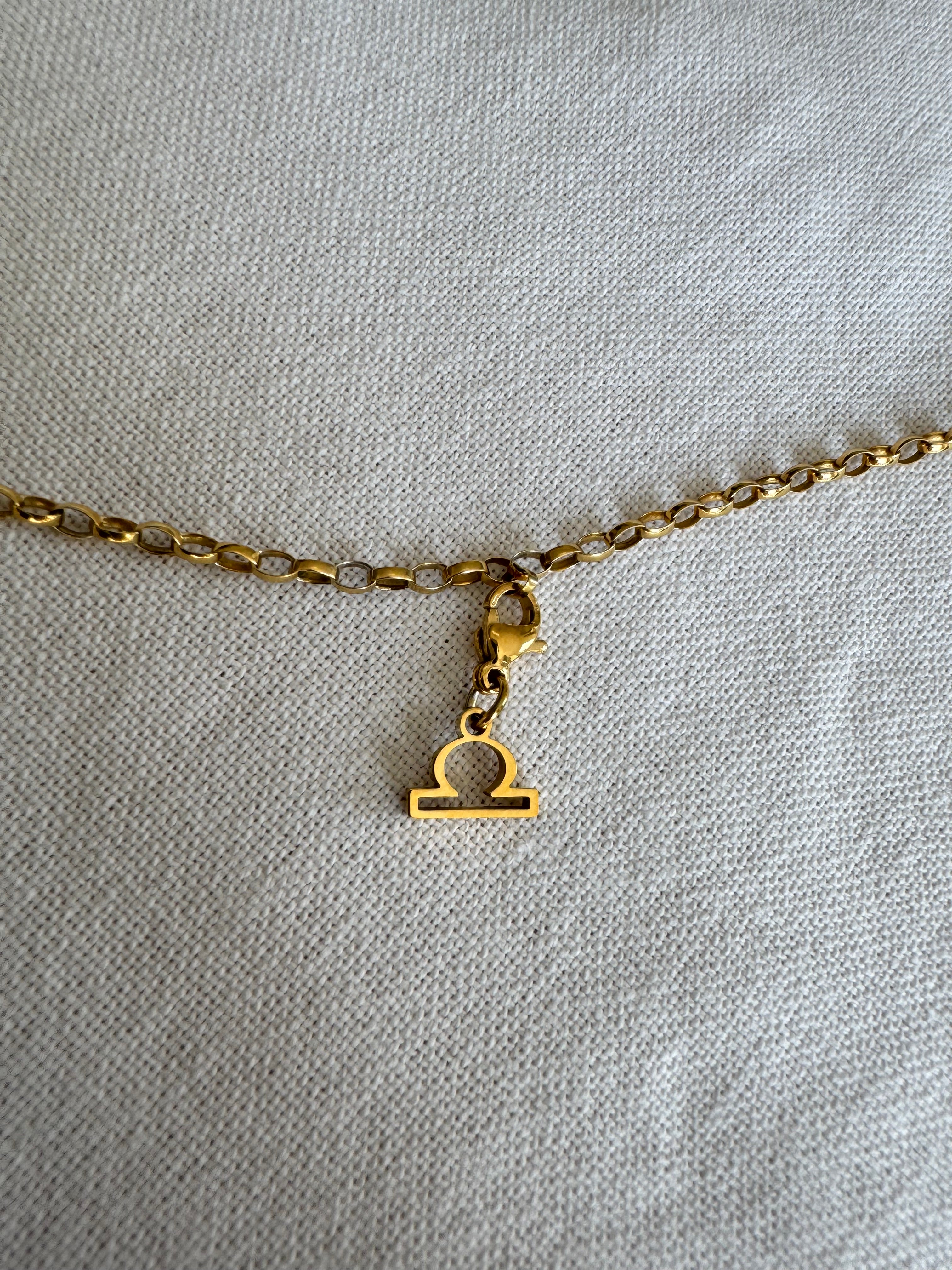 Goldener Waage Sternzeichen Charm an  goldenem Armband liegt auf weißem Leinentuch