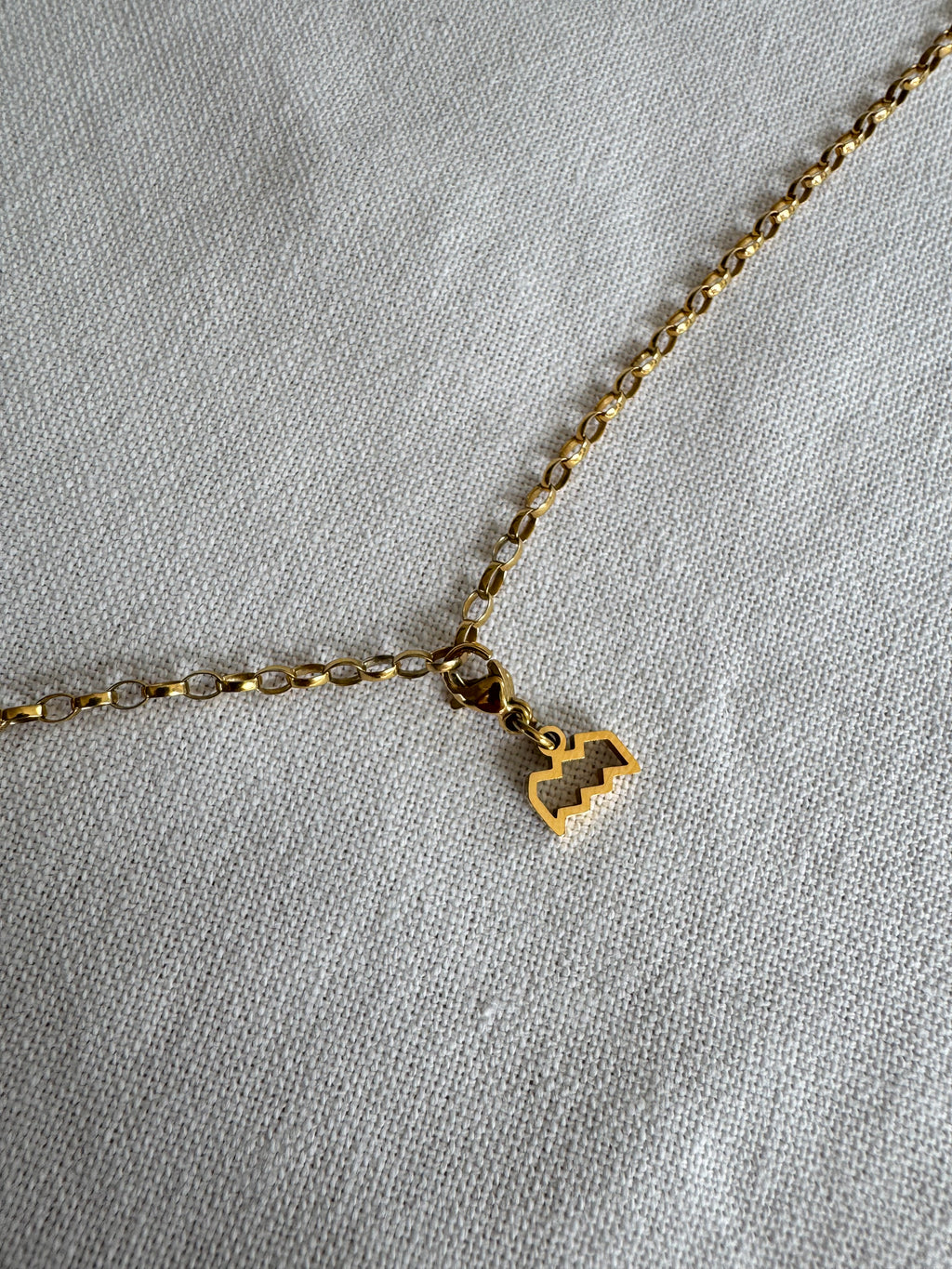 Goldener Wassermann Sternzeichen Charm an  goldenem Armband liegt auf weißem Leinentuch
