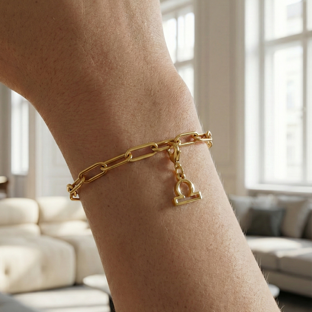 Charm Sternzeichen Waage in gold hängt an goldenem Armband am Handgelenk. Im Hintergrund stylische Altbauwohnung