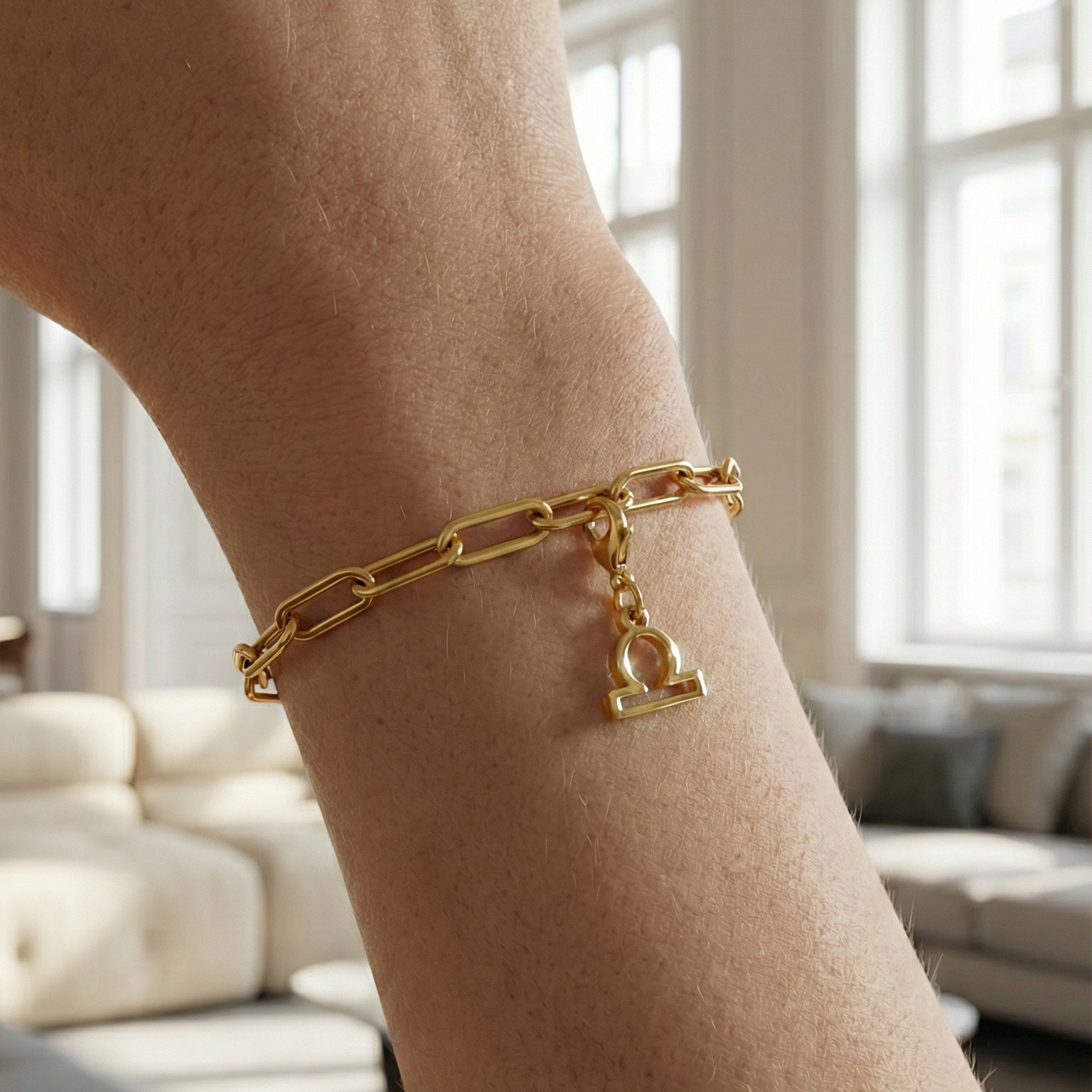 Charm Sternzeichen Waage in gold hängt an goldenem Armband am Handgelenk. Im Hintergrund stylische Altbauwohnung
