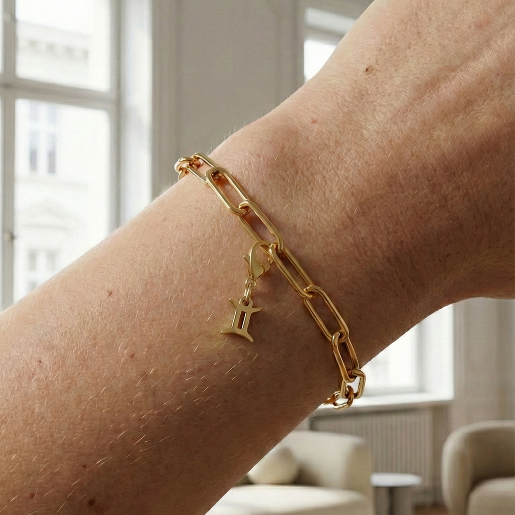 Charm Sternzeichen Zwilling in gold hängt an goldenem Armband am Handgelenk. Im Hintergrund stylische Altbauwohnung